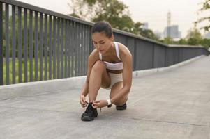 mujer joven fitness en ropa deportiva atando cordones de zapatos en el parque de la ciudad, saludable y estilos de vida. foto