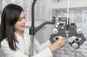 Young ophthalmologist doing visual test for customer using Bifocal Optometry eyesight measurement device in optical center, eyecare concept. photo