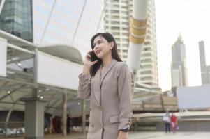 una joven y hermosa mujer de negocios está usando un teléfono inteligente en una ciudad moderna, tecnología de negocios, concepto de estilo de vida de la ciudad foto