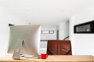 computadora del espacio de trabajo colocada en un escritorio de madera y rodeada de una taza de café, un portapapeles, una maceta, una pila de teléfonos inteligentes, tabletas y una oficina ordenada con teclado. foto