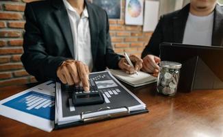 Business documents on office table with smart phone and calculator digital tablet and graph business with social network diagram and two colleagues discussing data working in office photo