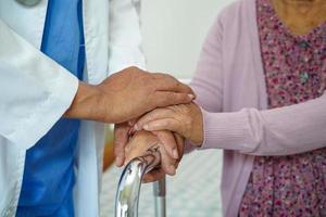 Doctor help Asian elderly woman disability patient walk with walker in nursing hospital, medical concept. photo