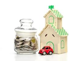 monedas en botella de vidrio y coche y casa sobre fondo blanco, ahorro empresarial y concepto de inversión foto