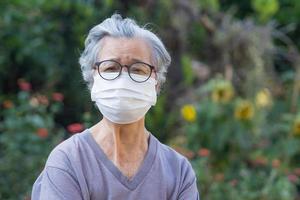 Elderly woman wearing a mask while standing in a garden photo