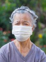 Elderly woman wearing a mask while standing in a garden photo