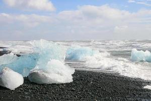 Black beach with big pieces of ice icebergs in the waves and on the edge of a cold sea in Iceland photo