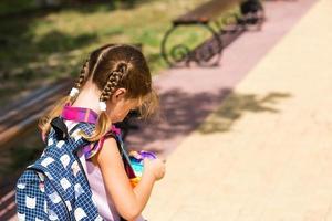 una niña pequeña con una mochila y un uniforme escolar en el patio de la escuela juega al juguete. regreso a la escuela, 1 de septiembre. el alumno se relaja después de las lecciones. educación primaria, clase elemental para estudiante foto