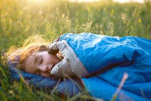 A child sleeps in a sleeping bag on the grass in a camping trip - eco-friendly outdoor recreation, healthy lifestyle, summer time. Sweet and peaceful sleep. Mosquito bites, repellent. photo