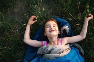 A child sleeps in a sleeping bag on the grass in a camping trip - eco-friendly outdoor recreation, healthy lifestyle, summer time. Sweet and peaceful sleep. Mosquito bites, repellent. photo