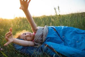 un niño duerme en un saco de dormir sobre la hierba en un viaje de campamento: recreación ecológica al aire libre, estilo de vida saludable, horario de verano. dulce y apacible sueño. picaduras de mosquitos, repelente. foto