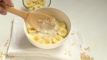 a man mixes oatmeal porridge with banana slices with a wooden spoon. video