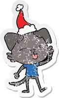 distressed sticker cartoon of a dog sticking out tongue wearing santa hat vector