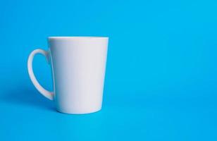 fotografía de la vista superior de la taza de café con leche en un platillo blanco el interior de la vitrocerámica parece vacío. esperando que se rellene el café caliente para beber para sentirse renovado y alerta sobre un fondo azul. foto