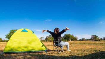 Asian female tourists are sitting happy free with green tent for traveler sits on  wide field, overlooking evening time Of Private area Thailand for camping getaway During long holiday for travel. photo