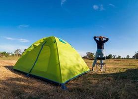 Asian female tourists are sitting happy free with green tent for traveler sits on  wide field, overlooking evening time Of Private area Thailand for camping getaway During long holiday for travel. photo