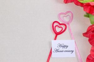 The plastic heart pairs with the happy anniversary card, with many flowers, brown background photo