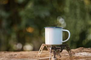 taza de café de esmalte blanco en la estufa de gas bosque verde bokeh background.vintage style. foto