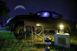 luz de lámparas de aceite antiguas, tetera en estufas de gas portátiles, mesas y sillas portátiles, vista nocturna con camionetas en el bosque. foto