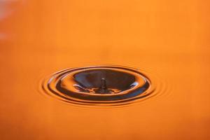gota de agua salpicada en un vaso de agua de color naranja que gotea y refleja agua. foto