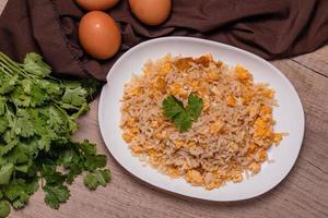 arroz frito con huevo de comida tailandesa en un plato blanco sobre un piso de madera foto