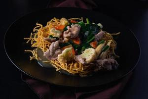 Crispy noodles with pork in a black plate. photo