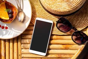 Empty screen smart phone with travel accessories on wooden table, Summer vacation concept photo
