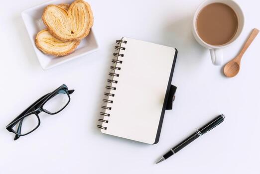 Cup of coffee with snacks and notebook on desk office with copy space, Top view photo