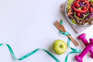 Fresh salad with green apple, dumbbell and measuring tape on white background. Diet, healthy eating concept photo