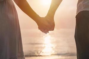 mujer joven viajera sosteniendo la mano del hombre y mirando hermosa puesta de sol en la playa, pareja de vacaciones en concepto de verano foto