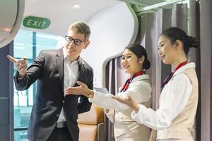 Flight attendant is welcoming and checking passenger boarding pass in business class and show him the way to his seat for airplane flight and airline transportation photo