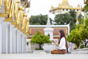 Asian buddhist woman is reading Sanskrit ancient palm leaf manuscript of Tripitaka the Lord Buddha dhamma teaching while sitting in temple on holy full moon day to chant and worship in the monastery photo