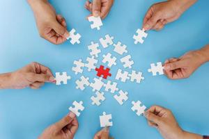 Hands of diverse people assembling jigsaw puzzle, team put pieces together searching for right match, help support in teamwork to find common solution concept, top close up view photo