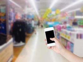 hand holding mobile phone with supermarket shelves aisle blurred background photo