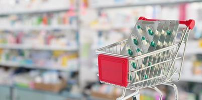 Medical pills capsule in shopping cart with pharmacy drugstore shelves blurred background photo