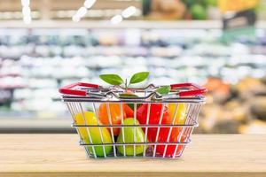 cesta de la compra con frutas en la mesa de madera sobre el fondo borroso del supermercado de la tienda de comestibles foto