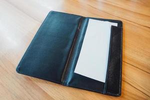 Blank empty white paper in black leather restaurant payment billing receipt folder on wood table photo