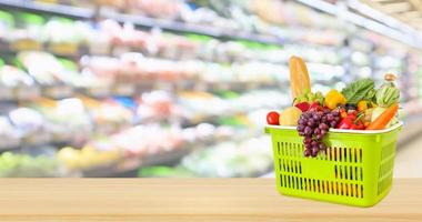 Shopping basket filled with fruits and vegetables on wood table with supermarket grocery store blurred defocused background photo