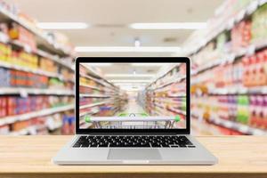 laptop computer on wood table with supermarket aisle blurred background online shopping concept photo