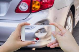 mujer que usa un teléfono inteligente móvil que toma una foto de un accidente automovilístico dañado para el seguro