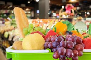 Shopping basket filled with fruits and vegetables with supermarket grocery store blurred defocused background with bokeh light photo