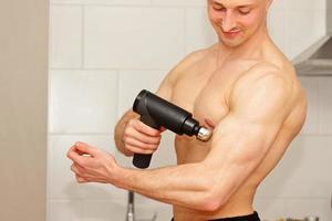 Sportsman with massage gun at home, photo