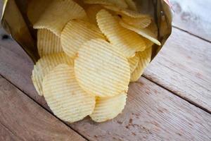 Opened pack with potato chips over wooden table photo