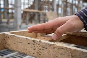 Trabajador de la construcción con la mano en el clavo en el sitio de construcción de la casa, concepto de accidente de trabajo foto