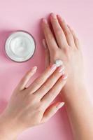 crema nutritiva y hermosas manos femeninas sobre fondo rosa. concepto de cuidado de la piel. imagen para publicidad y diseño. foto