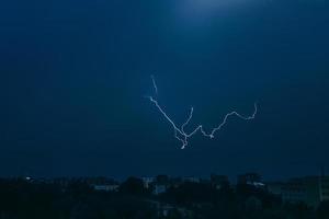 Lightning in sky over city. Bright flashes on dark night. Thunderclouds and electricity discharges in  atmosphere. photo