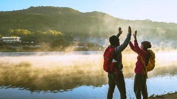 mujer asiática y hombre asiático que mochilero de pie cerca del lago, ella estaba sonriendo, feliz y disfrutando de la belleza natural de la niebla. foto