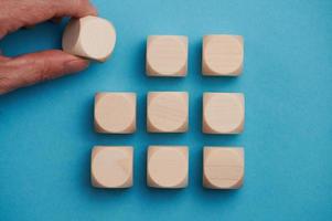 nine wooden cubes on blue background, one will be added by a female hand photo