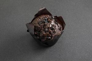 Chocolate muffin in brown paper cup with chocolate pieces on black background photo