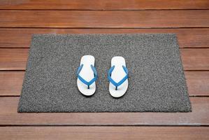 Dark gray doormat with white slippers on wooden floor photo