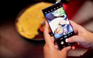 mujer sosteniendo un teléfono inteligente y tomando una foto con la comida de vietnam para mostrarla en sus redes sociales.